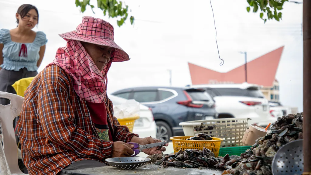 A local vendor shelling green mussels in Sriracha