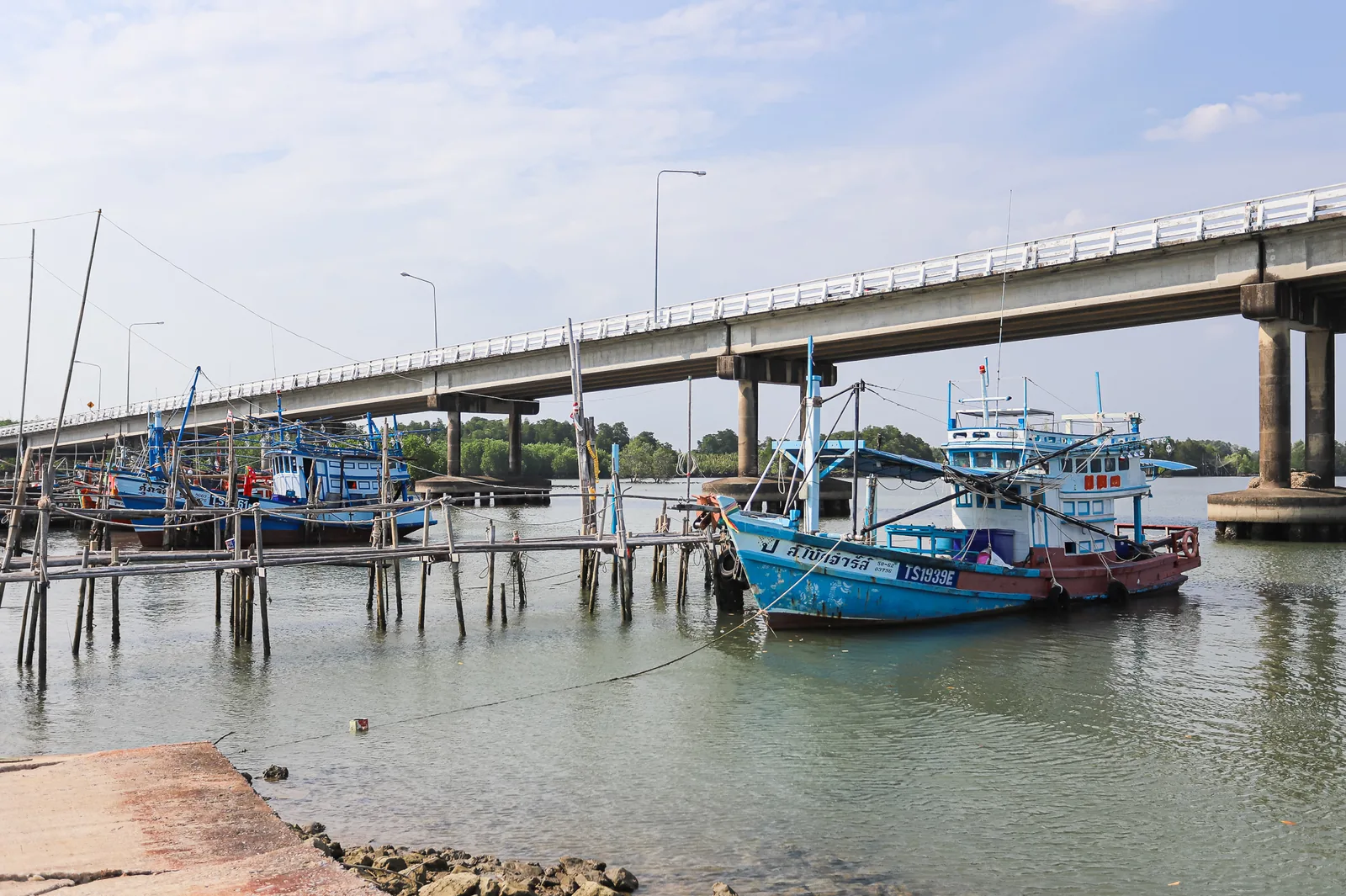 Thai fishing boats with registration numbers on their hulls, moored at Ban Laem Sing pier beside a bridge, Chanthaburi
