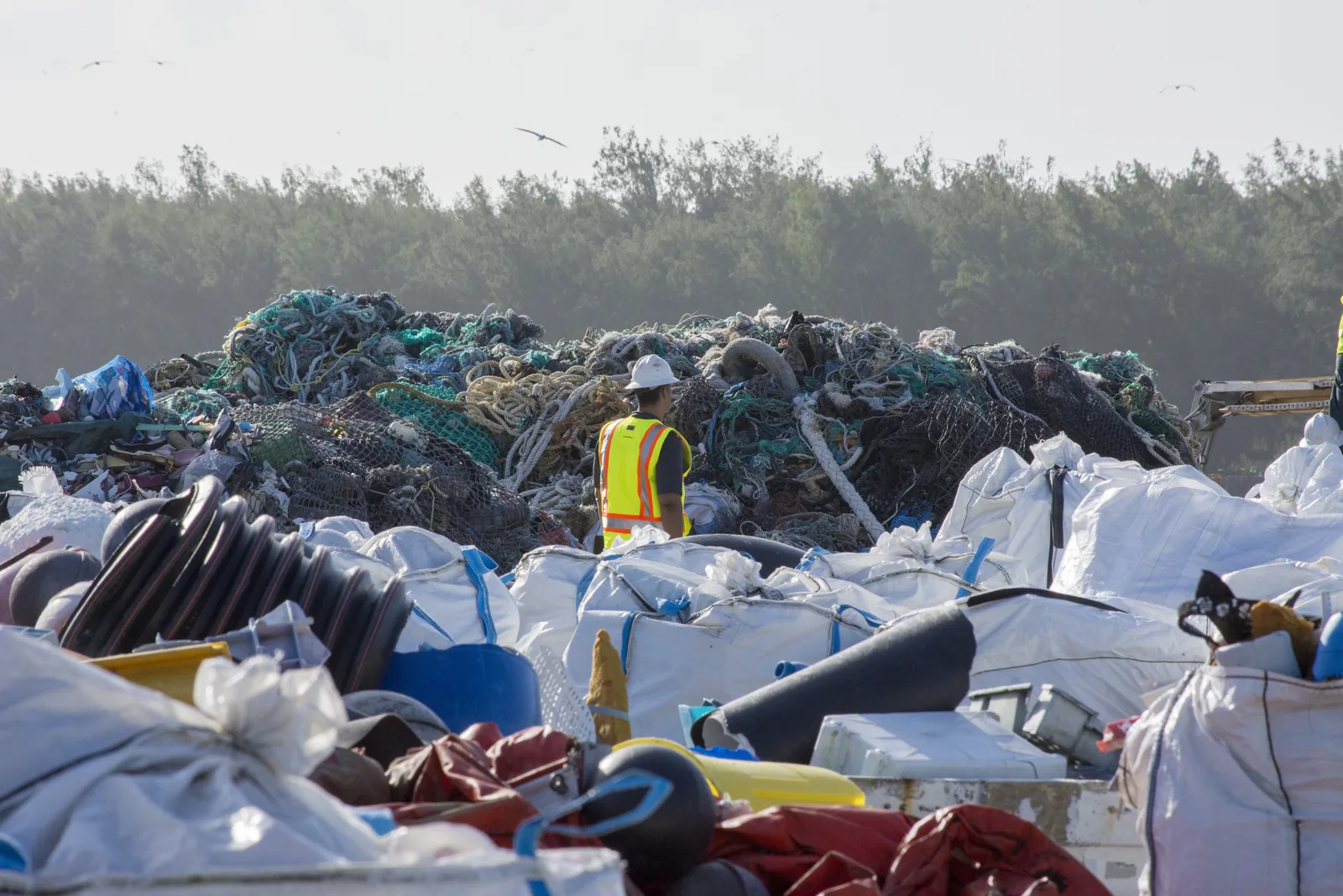 Worker among piles of nets, plastic and other marine debris collected on Midway Atoll